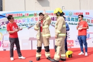 伍允龙（左二）穿上抗火衣「黄金战衣」，并由消防队目介绍「黄金战衣」的功能及穿着技巧，让观众了解消防员的装备。